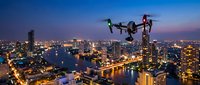 Modern drone flying over illuminated city skyline at dusk with river and urban lights creating stunning aerial photography perspective for commercial use.