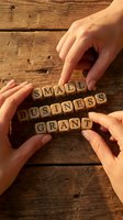 Hands arranging wooden letter cubes spelling small business grant on a rustic wooden table, symbolizing funding and entrepreneurship support.