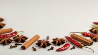 Aromatic spices including cinnamon sticks, star anise, dried chili peppers and cloves arranged on white background for culinary and cooking projects.
