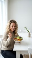 Happy blonde woman enjoying healthy salad bowl in bright modern kitchen. Nutritious eating lifestyle concept for wellness and diet content.