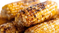 Grilled corn on cob with butter and spices in macro shot showing detailed texture of charred kernels, melted seasoning and grill marks for food photography.