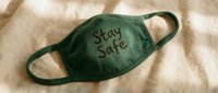 Green fabric face mask with Stay Safe text lying on linen background, health protection and safety awareness concept.