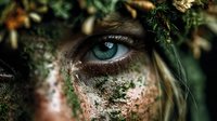 Mystical forest goddess with piercing blue eyes surrounded by moss and natural elements creating ethereal fantasy portrait for creative projects.