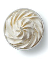 Creamy white frosting swirled in decorative pattern in round bowl isolated on white background for baking and dessert preparation.
