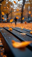 Orange autumn leaves falling on wet park bench during light rain, creating moody atmospheric scene with bokeh effect and selective focus on wooden slats.