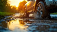 Car wheel splashing through muddy puddle at sunset with dramatic water spray and reflection on wet ground, creating dynamic off-road adventure scene.