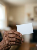Senior man with dark skin holding blank white card indoors, suitable for business cards, invitations, announcements, and promotional materials.