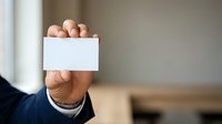 Man in business attire holding blank white card at chest level, displaying empty space for text or branding in corporate setting.