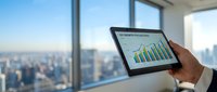 Young male professional of mixed ethnicity holding tablet displaying financial growth charts in modern high-rise office with panoramic city skyline view, representing business analytics and data analysis.