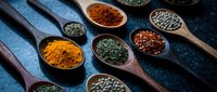 Colorful spices and herbs in wooden spoons on dark blue textured surface. Turmeric, paprika, peppercorns, seeds arranged for culinary cooking and seasoning.