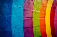 Vibrant rainbow stripes painted on textured concrete wall creating colorful urban background with deep blue, turquoise, purple, yellow, and red gradient bands.