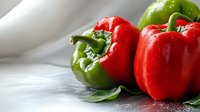 Fresh red and green bell peppers on white wooden surface with natural lighting for healthy cooking and meal preparation.