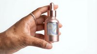 African American woman hand holding rose gold perfume bottle with holographic label against white background for beauty and fragrance advertising.