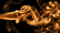 Glowing golden smoke swirls gracefully against a dark black background, creating an abstract fiery wave pattern for creative design use.