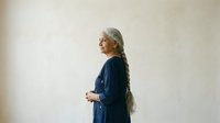 Senior woman with gray hair wearing dark blue cardigan standing against neutral wall, side profile view for healthcare, wellness, aging, lifestyle and portrait concepts.