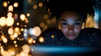 Young African American woman using tablet computer at night with warm bokeh lights creating magical atmosphere for digital lifestyle and technology.
