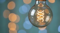 Vintage Edison bulb with spiral filament glowing warmly against colorful bokeh lights background creating cozy atmospheric lighting for home decor and design projects.