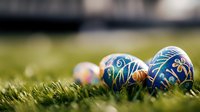 Decorated Easter eggs with intricate blue and gold patterns lying on fresh spring grass in soft natural lighting, creating festive holiday atmosphere.