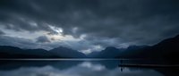 Dramatic stormy clouds over serene mountain lake with perfect reflections creating moody atmospheric landscape scene for nature and travel content.