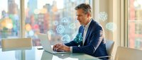 Middle-aged Caucasian businessman in navy suit working on laptop with digital network icons in modern office with autumn city view through windows.