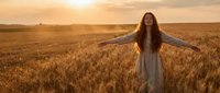 Young woman with long hair embracing freedom in golden wheat field at sunset, arms outstretched in peaceful moment of joy and connection with nature.
