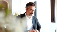 Mature businessman with salt and pepper hair working on laptop in bright office space, focused on professional task.