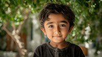Young Hispanic boy with curly hair smiling warmly at camera in natural outdoor setting with green foliage background for family and childhood concepts.