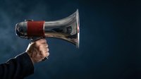 Businessman shouting through megaphone against dark background with dramatic lighting for communication and leadership concepts.