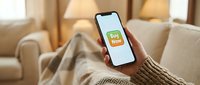 Hand holding smartphone with Buy Now button on screen, online shopping concept in cozy home interior, e-commerce and mobile retail.