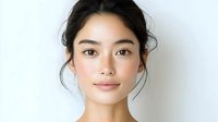 Young Asian woman with natural makeup and dark hair in messy updo poses against white background, looking directly at camera with serene expression.
