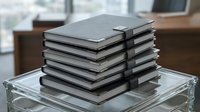 Stack of sleek modern laptops piled on glass table in contemporary office environment for technology and business concepts.