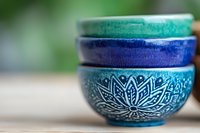 Stacked ceramic bowls with lotus pattern in turquoise and deep blue glazes, showing traditional artisanal craftsmanship against soft blurred background.
