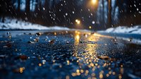 Raindrops falling on dark wet asphalt surface with golden bokeh lights reflection creating atmospheric moody evening scene during rainfall in city street.