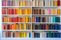 Colorful bookshelf with books arranged by spectrum colors from pink to blue, creating rainbow effect on white shelving unit for home library or bookstore display.