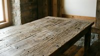 Rustic wooden table with weathered surface and natural grain texture, set in industrial loft space with exposed brick and wooden beams, suitable for interior design and furniture photography.
