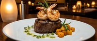 Grilled steak topped with two succulent shrimp, served with roasted vegetables and herb garnish on elegant white plate in fine dining restaurant setting.