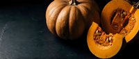 Fresh orange pumpkin cut in half showing seeds and flesh on dark background for autumn cooking and Halloween decoration projects.