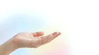 Open palm of a woman with light skin tone, facing upward in a gentle, welcoming gesture against a soft, blurred background with warm peachy and cool blue tones.