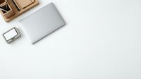 Modern workspace flat lay with closed laptop, smartphone and wooden organizer on clean white desk surface for business and productivity concepts.