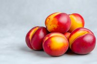 Fresh ripe nectarines with red and yellow skin on light gray background, macro food photography for healthy eating and summer fruit concepts.