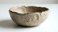 Rustic handmade ceramic bowl with rough textured surface isolated on white background, showcasing artisan craftsmanship and natural earthy tones.