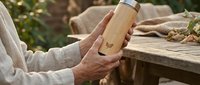 Hands holding eco-friendly bamboo water bottle outdoors on wooden table. Sustainable lifestyle and zero waste concept for environmental awareness.