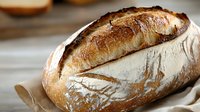 Freshly baked artisan sourdough bread with golden crust and rustic texture, served on parchment paper for bakery display or food photography.