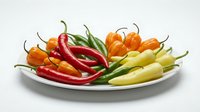Colorful assorted hot chili peppers arranged on white plate including red, orange, yellow and green varieties for cooking and spice preparation.