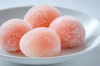 Pink mochi balls dusted with powdered sugar served on white ceramic plate, traditional Japanese dessert with soft and chewy texture, close up view.