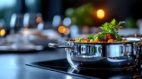 Steaming pot with fresh vegetables and herbs on modern induction cooktop, soft bokeh lights creating cozy restaurant atmosphere. Professional culinary scene.