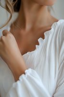 Elegant close-up of a young Caucasian woman in white pleated dress with ruffled neckline, showing graceful neck and shoulder pose against neutral background.