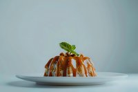 Elegant molded dessert with glossy caramel sauce and fresh mint garnish on white plate against soft gray background for culinary presentations.