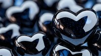 Glossy black heart shapes with reflective surfaces arranged in rows create romantic pattern. Dark mysterious background adds dramatic mood for valentines designs.