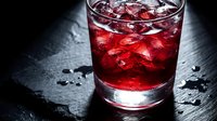Red cocktail with ice in a rocks glass on dark slate surface, dramatic moody lighting for bar menu or beverage advertising.